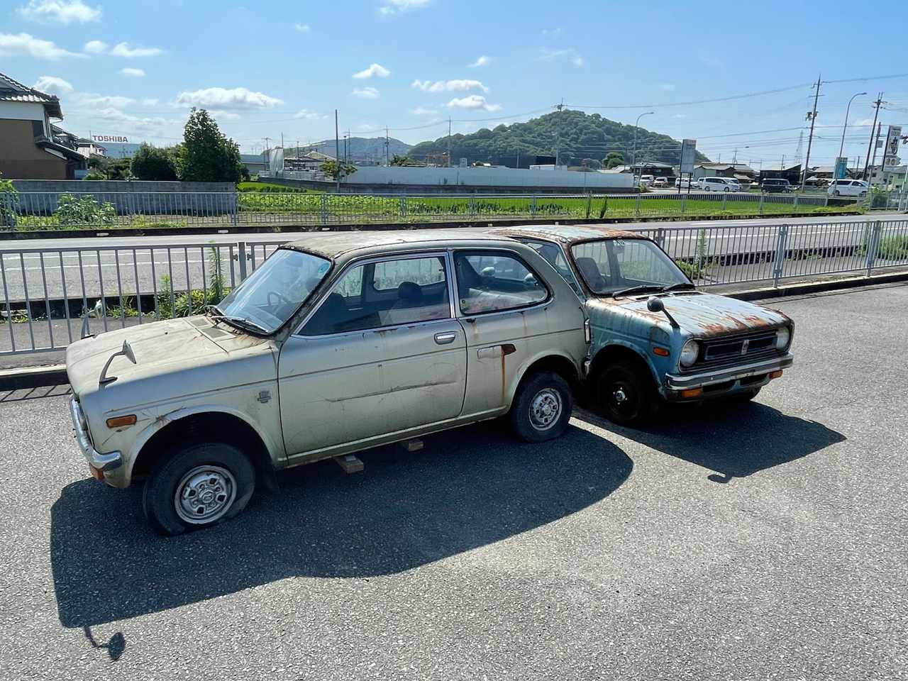 整備中の白いフォルクスワーゲン・ビートルと、屋外に並ぶ年式の古い小型車。