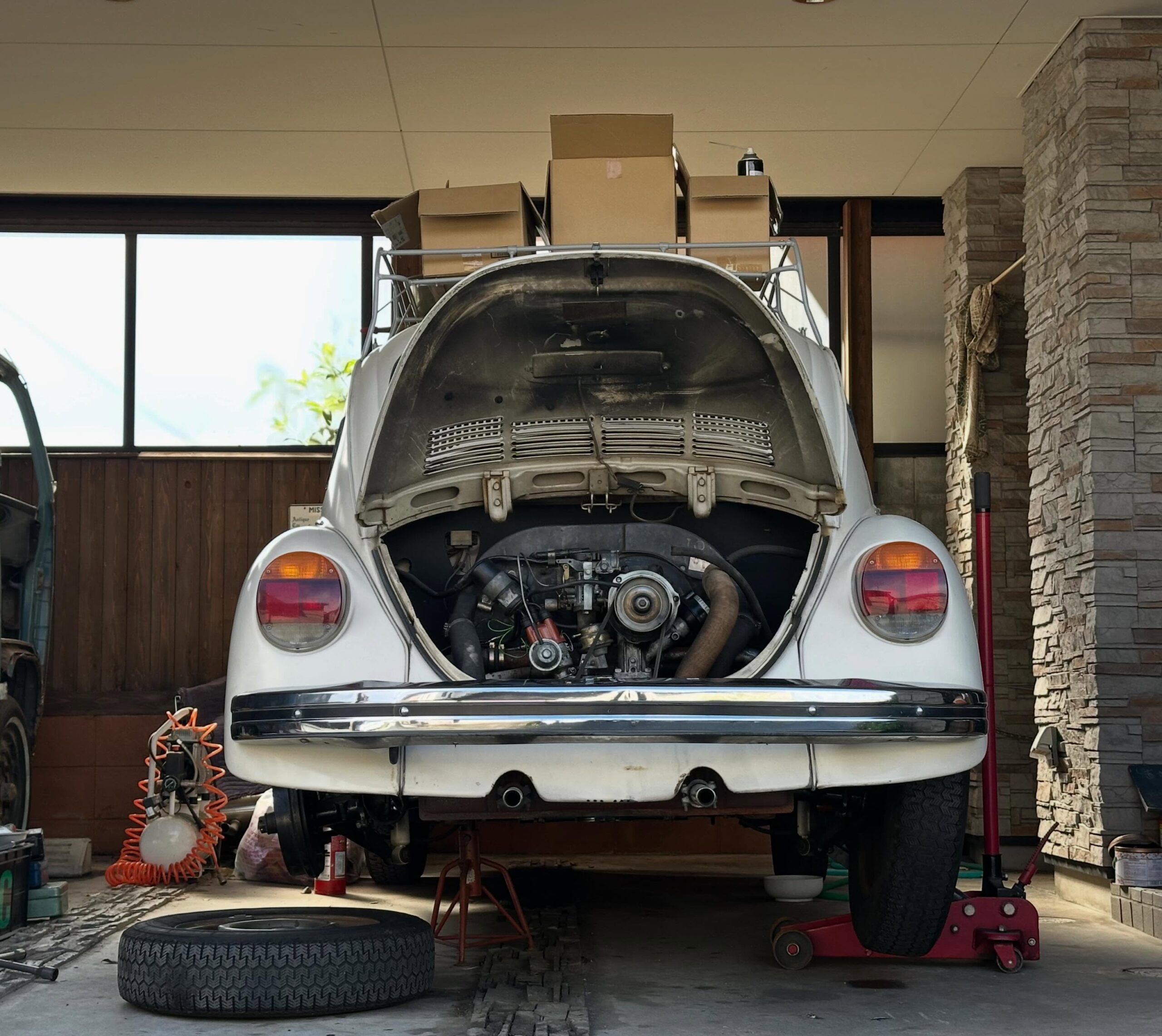整備中の白いフォルクスワーゲン・ビートルと、屋外に並ぶ年式の古い小型車。