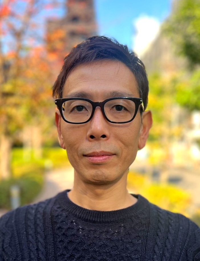 屋外でカメラを見る細谷健一さんのポートレート