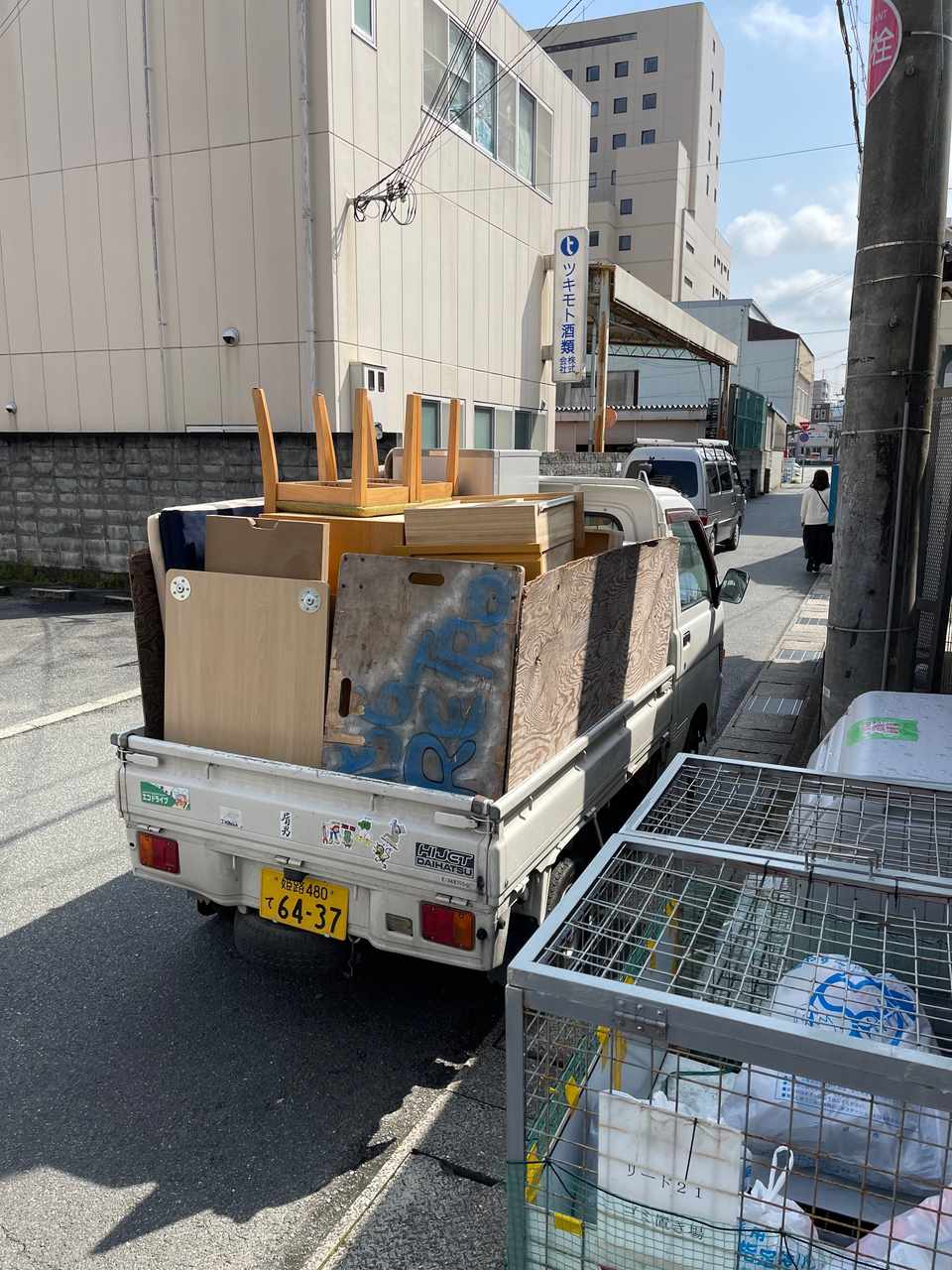 建物前に停車した軽トラックの荷台に、家具や家電などの回収品が積み込まれている不用品回収の現場。