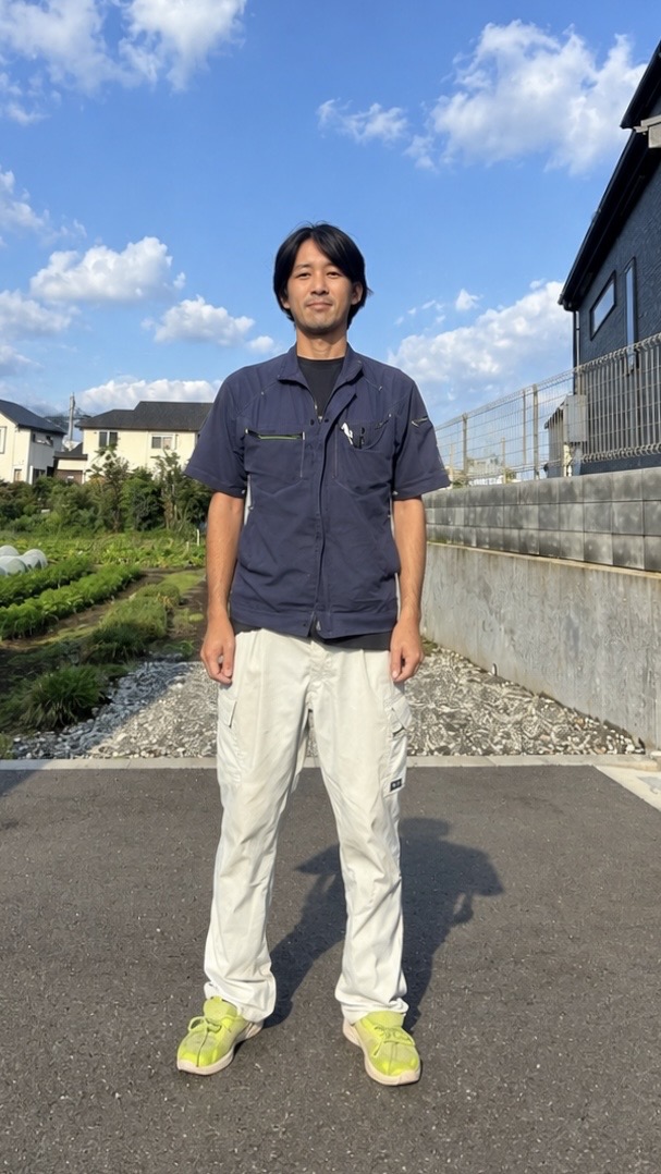 屋外に立つ作業着姿の田島さんと、ケーブルや工具箱、測定機器を整理して積載した田島電気設備の作業車両後部