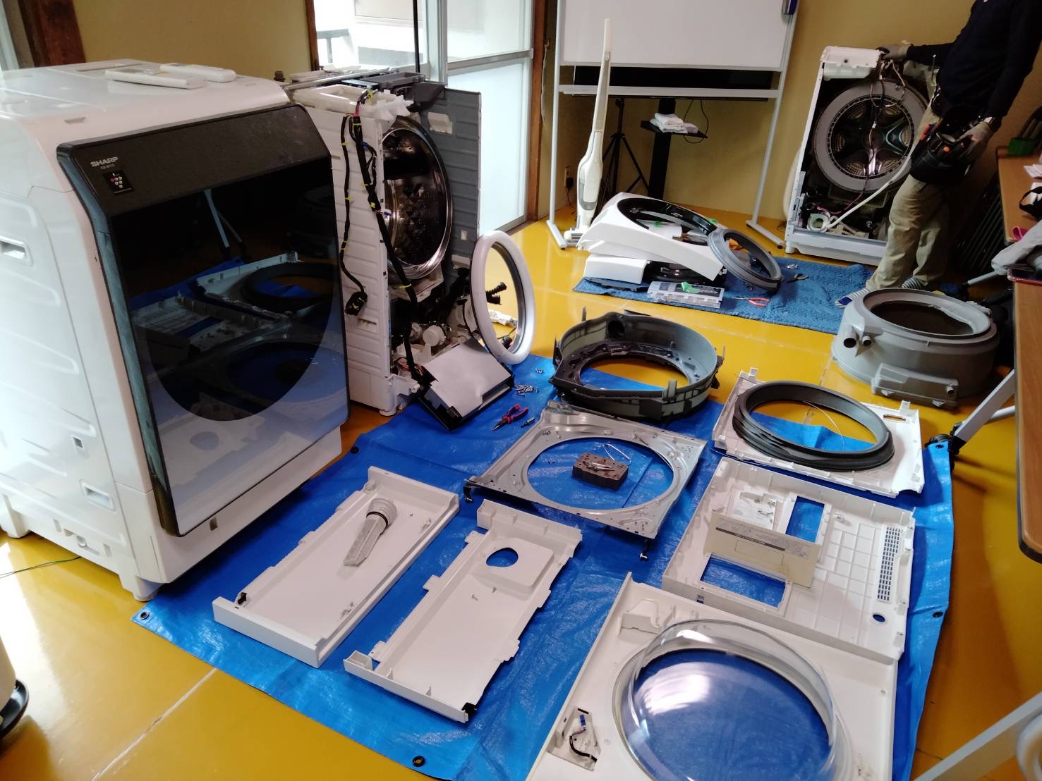 分解して部品を並べたドラム式洗濯機の修理現場