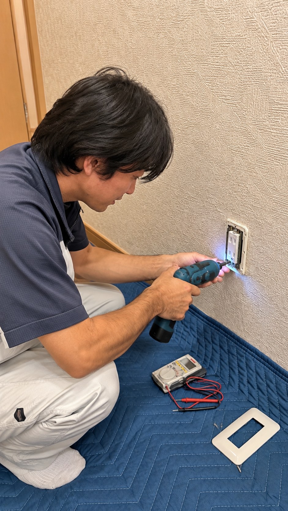 壁面の電気設備を電動工具で施工する田島さん