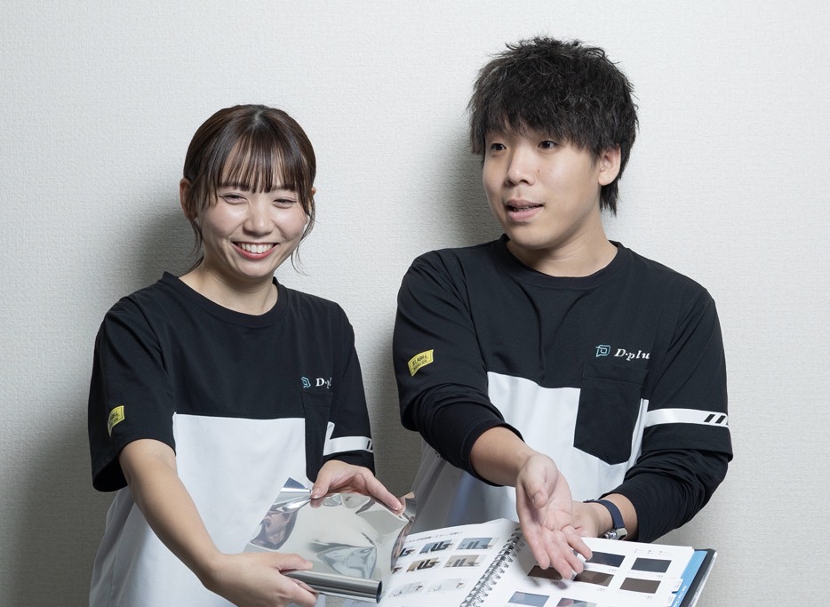 窓ガラスフィルムの見本帳を示す中谷さん夫妻と、大きな窓から見える街並み