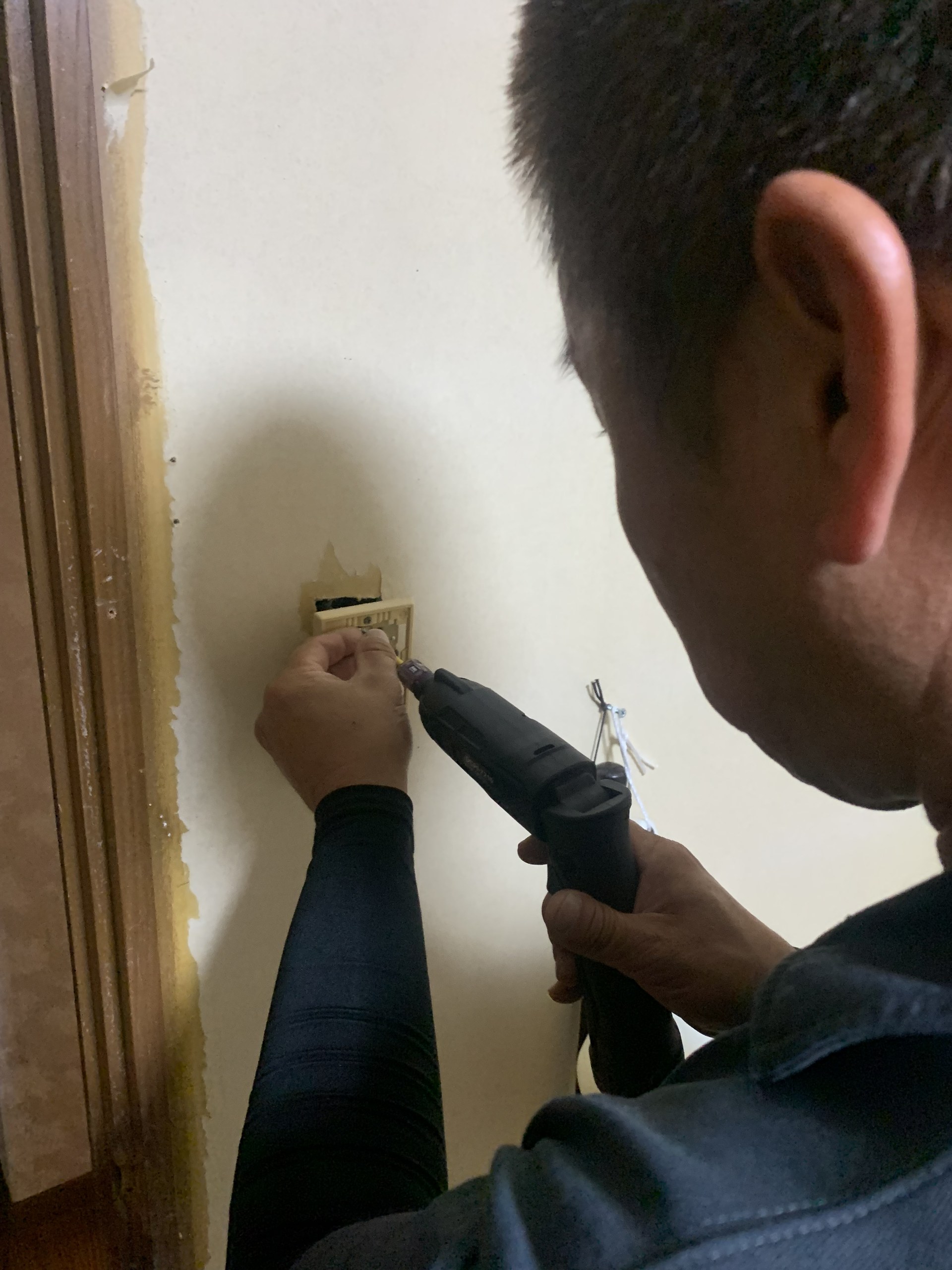 壁の電気設備に電動工具で作業する山本さん