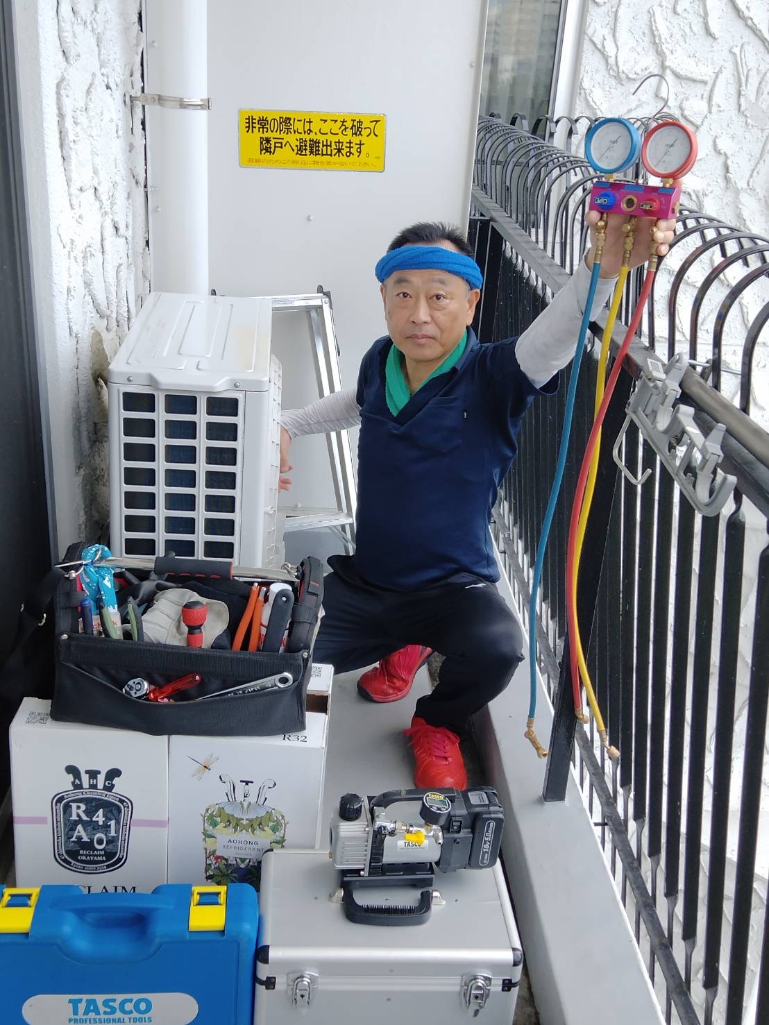 修理機材と室外機のそばで作業する猪俣さん